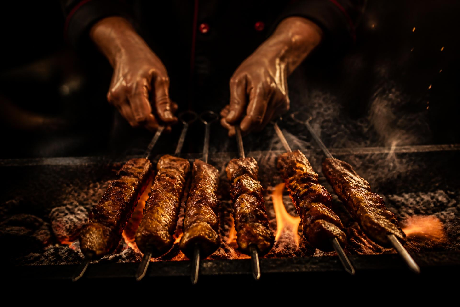 Chef turning marinated skewers over a live charcoal grill